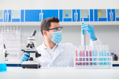 Bilimsel meydan okuma. Şişe yükseltirken ve ona bakarken güvenlik gözlükleri içinde Hoş yakışıklı erkek laboratorian soyunma