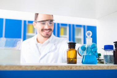Lab inside. Selective focus of male hand taking lab glasses with liquids poured in and standing on surface