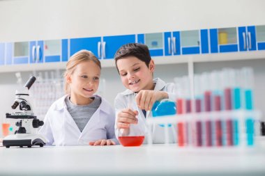 Genç kimyagerler. Neşeli pozitif zeki çocuklar birlikte ayakta ve kimya okurken bir deney yürüten