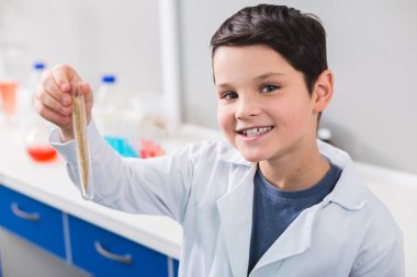 Boşuna kırpma. Akıllı iyi görünümlü memnun çocuk kameraya bakarken şişe tutan ve laboratuvar önlüğü giyen