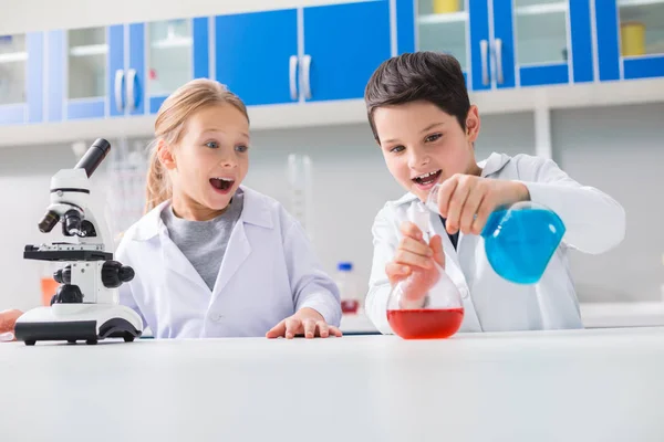 Interesting chemistry. Positive joyful smart boy holding flasks and mixing chemical reagents while being in the lab