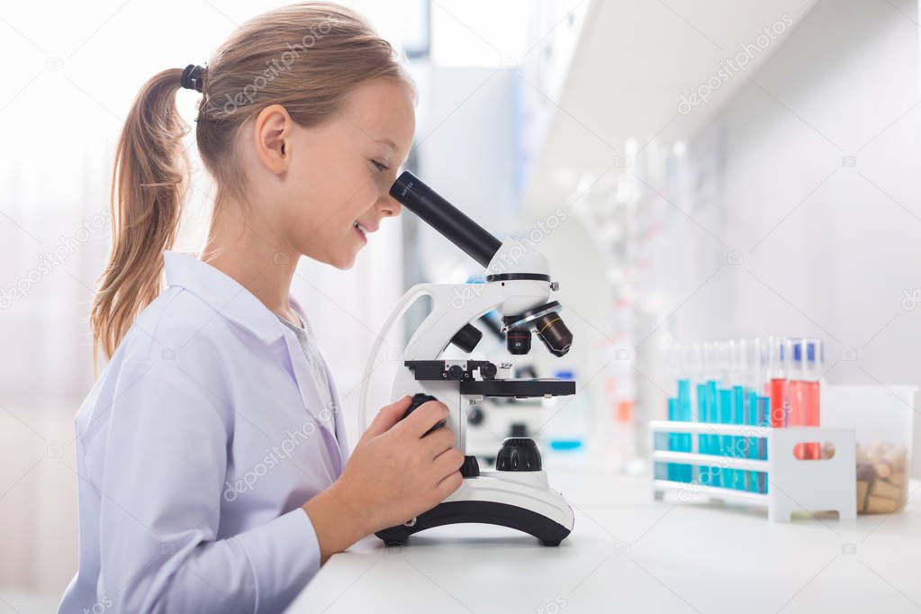 Great instrument. Appealing ambitious beautiful girl posing in profile while looking in microscope and touching it
