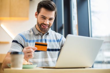 Elektronik bankacılık. Bir kredi kartı tutan ve bir online ödeme yaparken gülümseyen Pozitif mutlu genç adam