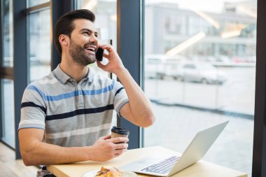 Hoş bir sohbet. Olumlu mutlu güzel adam kafede oturan ve hoş bir telefon görüşmesi yaparken gülüyor