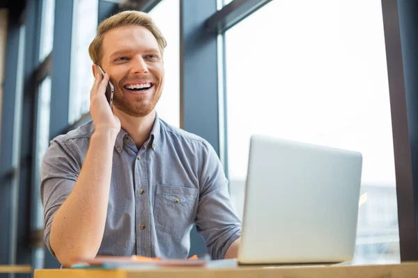 İyi bir ruh hali. Neşeli pozitif güzel adam kulağına cep telefonu koyarak ve hoş bir konuşma yaparken gülüyor