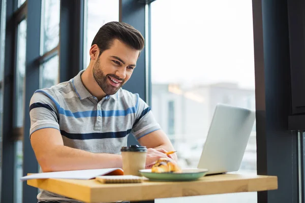 Involved in work. Smart positive handsome man sitting at the table in the cafe and having lunch while being involve in his work