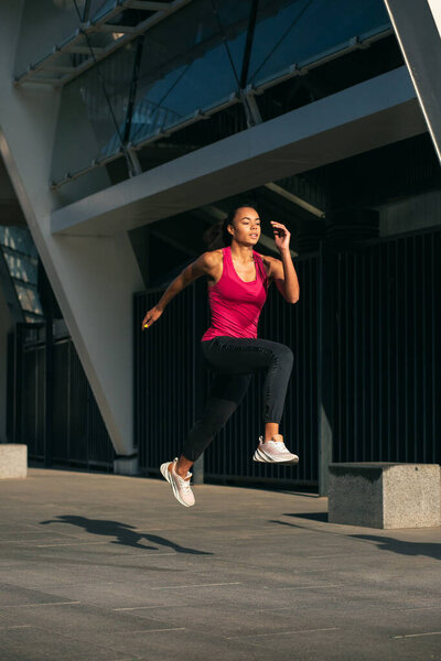 Городское фото с бегущей спортивной женщиной и находящейся в воздухе в движении
