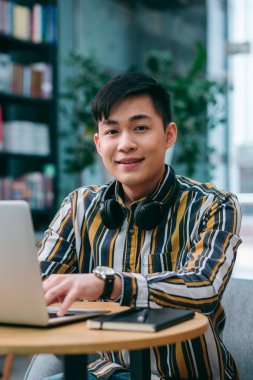 Masada dizüstü bilgisayarı olan neşeli genç bir adam oturuyor ve mutlu görünüyor.