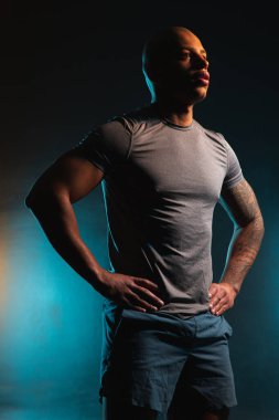 Sakin genç adam ellerini beline koyar ve başka yere bakar.