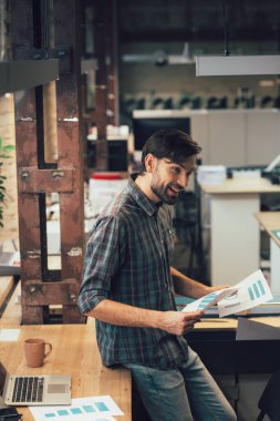 Masanın yanında elinde belgelerle bekleyen çekici genç bir adam.