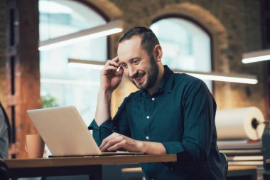 Pozitif genç çalışan, iş yerindeyken ekrana bakıp gülümsüyor.