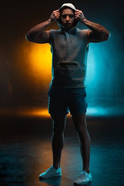 Ciddi bir adam stüdyoda turuncu bir arka planda dururken kafasına bir başlık geçirir.