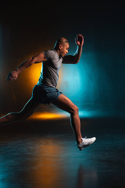 Determined sportsman running fast. Studio photo with orange and teal light on background