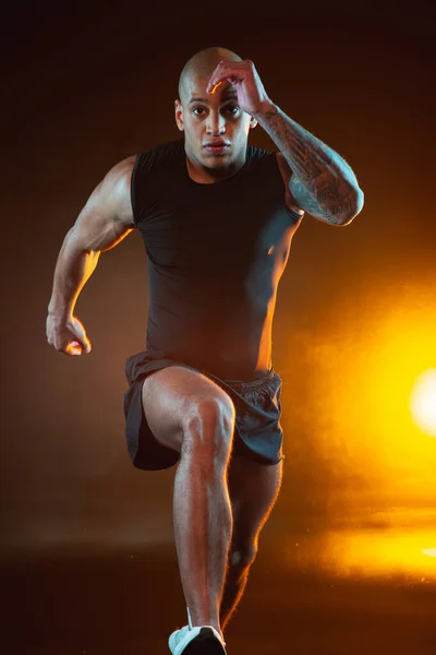 走っている間に集中しているように見える大胆なスポーツマンを入れ墨 後ろのオレンジの光 — ストック写真