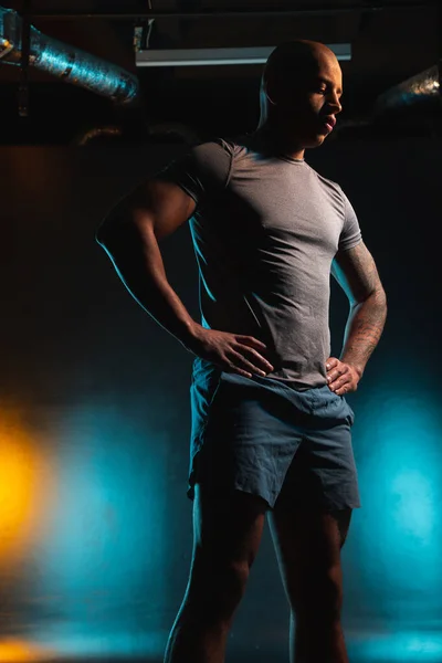 Young bold man in shorts and T shirt standing with his hands on the waist and looking down