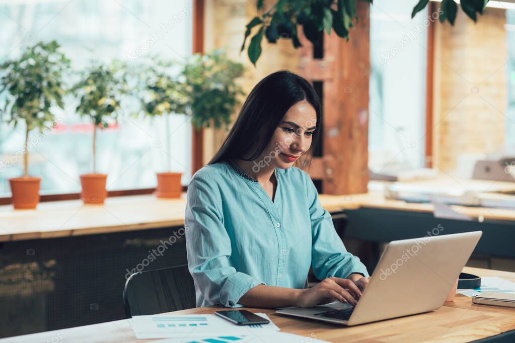 Calm smiling woman using a laptop for work while sitting at the table