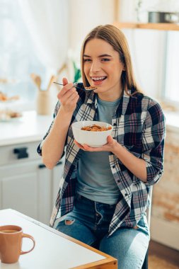 Mutfakta bir kase mısır gevreğiyle gülümseyen kadın.