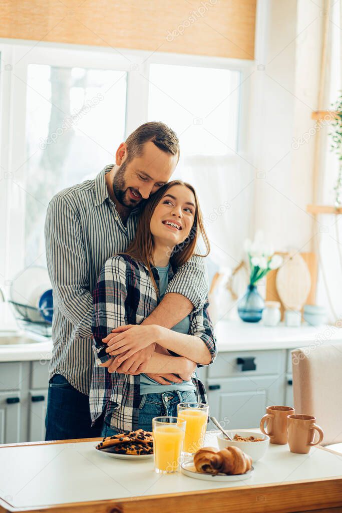 Loving man hugging his beautiful girlfriend in the kitchen. Breakfast in front of them