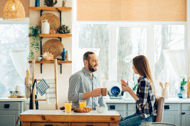 Gülümseyen güzel bir çift. Gündüz mutfakta oturup yemek yerken sohbet ediyorlar.