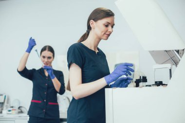Neşeli laboratuvar asistanları gülümsüyor ve modern laboratuvar ekipmanları ve örnekleriyle çalışıyor.
