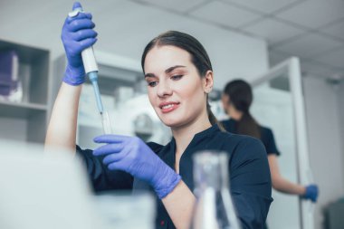 Deney tüpüne sıvı atarken gülümseyen kendinden emin laboratuar bilimcisi.