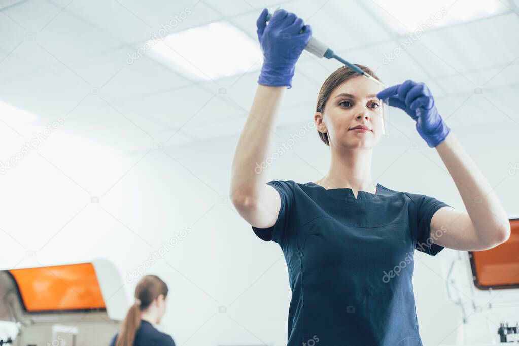 Calm lab assistant wearing rubber gloves standing with a test tube and a dropper