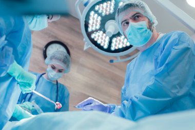 Tıbbi maskeli ciddi bir doktor neşter tutuyor ve meslektaşlarıyla cerrahi operasyonlar yapıyor.