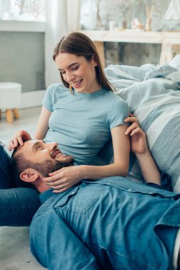 Neşeli bayan oturuyor ve kucağında yatan pozitif erkek arkadaşına nazikçe gülümsüyor.