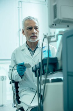 Kendine güvenen olgun bir doktor ultrason tarayıcısıyla monitörün önünde oturuyor.