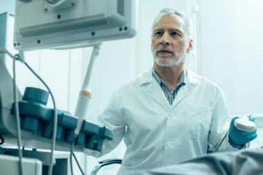 Kendine güvenen olgun bir adam ultrason taraması sırasında dikkatlice ekrana bakıyor.