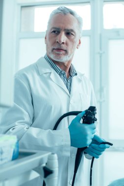 Plastik eldivenli bir tıp çalışanı elinde bir endoskop tutarak ekrana doğru dönüyor.