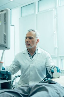 Ciddi bir sağlık çalışanı ultrason taraması yapıyor ve ekrana dikkatlice bakıyor.