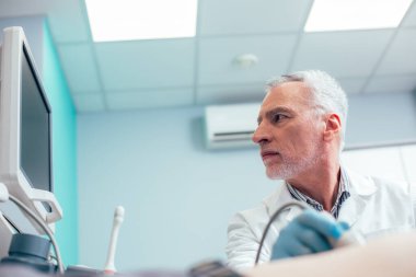 Kendine güvenen doktor başını monitöre çeviriyor ve ultrason çevirici kullanıyor.