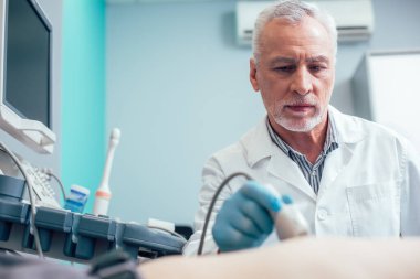 Sakin doktor, elinde ultrason dönüştürücü ve tomografi tomografisi tutan lastik eldivenli.