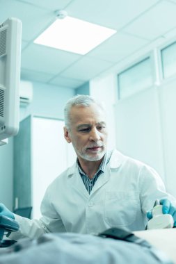 Sakin, olgun bir doktor hastanın yanında oturuyor ve ultrason cihazıyla midesini tarıyor.