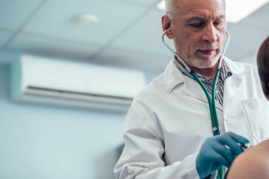 Bir hastanın akciğerlerini kontrol ederken steteskop kullanan sakin bir doktoru kapatın.