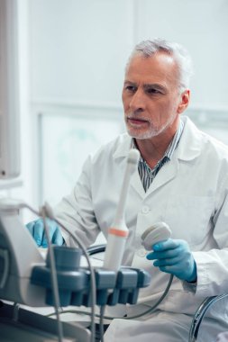 Yoğunlaşmış erkek doktor modern ultrason cihazlarının monitörünün önünde oturuyor.