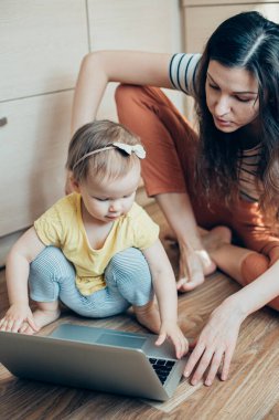 Sakin bir kadın yerde oturuyor ve bilgisayarını kızından geri almaya çalışıyor.