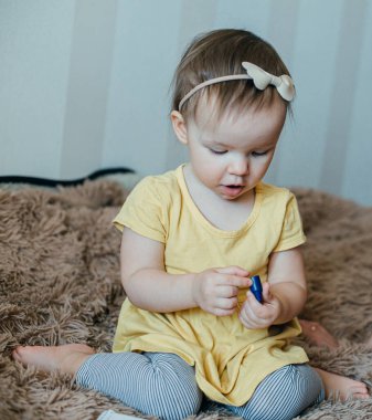 Sevimli küçük kız elinde mavi bir pastel boyayla çıplak ayakla yatakta oturuyor.