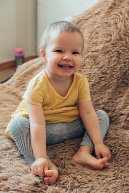Yumuşak kabarık bir battaniyenin üzerinde otururken gülümseyen yalınayak tatlı bebek.