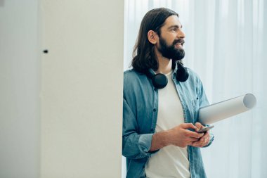 Boynunda kulaklığı olan neşeli genç bir adam elinde bir rulo kağıt ve akıllı bir telefon tutuyor. Şablon pankartı