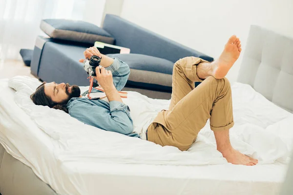 Jovem Calmo Deitado Cama Ajustando Configurações Uma Câmera Suas Mãos — Fotografia de Stock