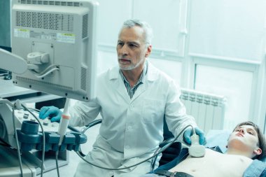 Olgun profesyonel doktor ultrason tarayıcısı kullanıyor ve ekran görüntülerine bakıyor.