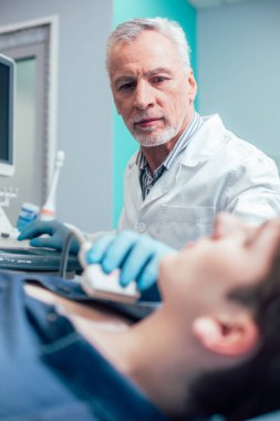Lastik eldivenli doktor, ultrason cihazıyla hastanın boynuna dokunuyor.