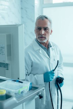 Modern bir endoskop tutan ve ekrana bakan kendinden emin yaşlı doktor.