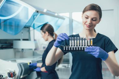 Test tüpü askısıyla dikilen ve dikkatlice test tüpüne dokunurken gülümseyen genç laboratuvar asistanı.