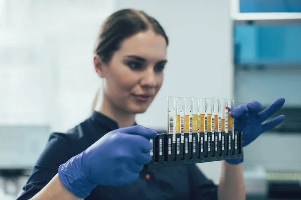 Lastik eldivenlerin içinde durup tüpler içindeki sıvılara bakan laboratuvar asistanına dikkat et.