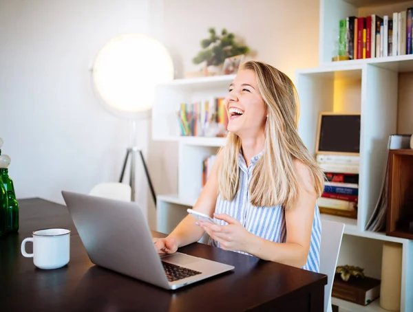 Mujer joven y feliz mirando su móvil mientras trabaja en casa — Foto de Stock