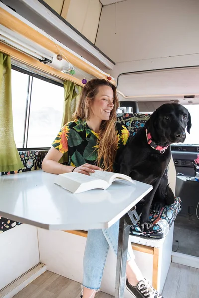 Feliz jovem mulher lendo um livro e brincando com seu cão em um c — Fotografia de Stock