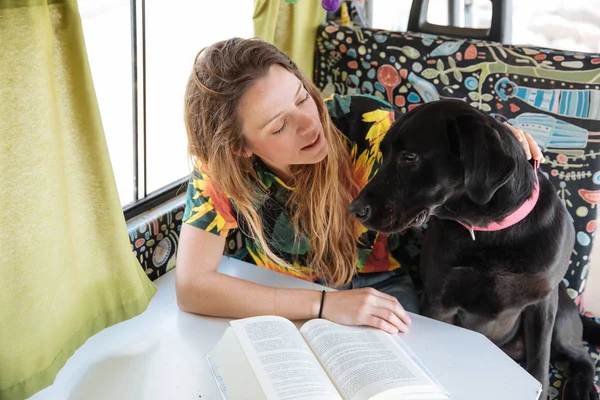 Feliz jovem mulher lendo um livro e brincando com seu cão em um c — Fotografia de Stock